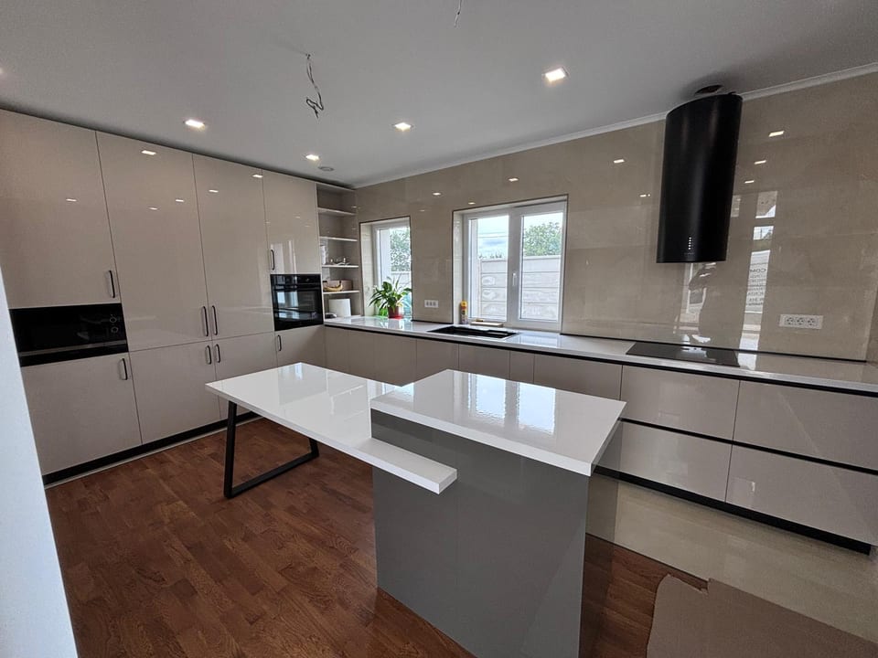 Bucătărie bej lucioasă cu insulă albă și mobilier până aproape de tavan