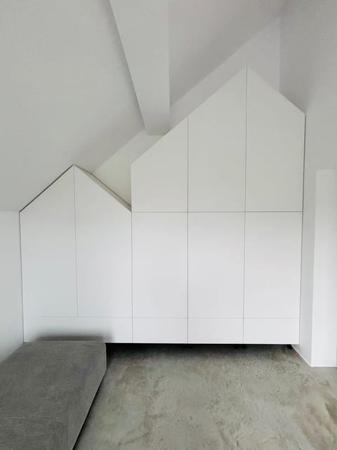 Mobilier alb realizat sub o scară, cu fronturi adaptate pantei